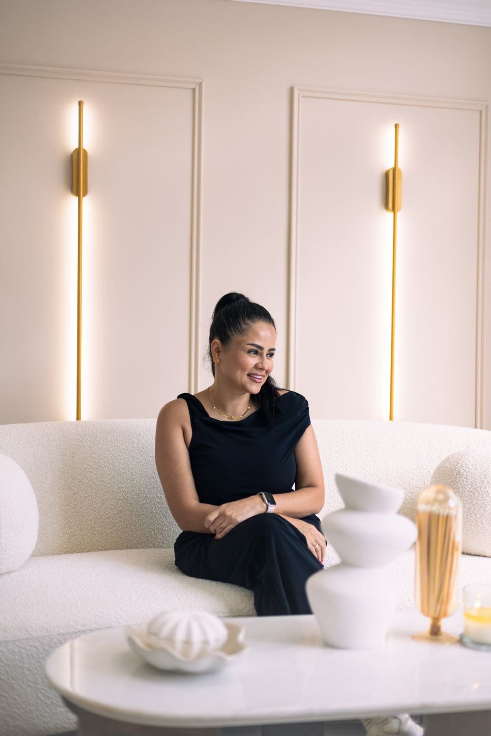 The founder of Lana Beauty & Aesthetics, seated smiling on a cream sofa in the clinic lounge.
