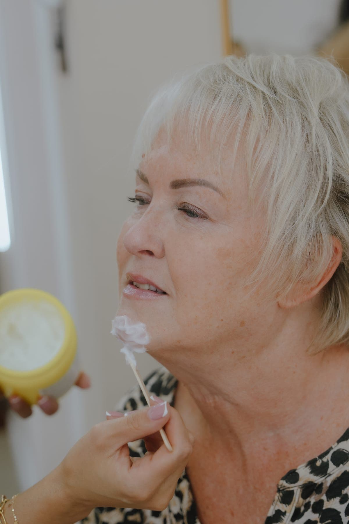 A client reclining during a facial treatment, skincare applied in careful lines across the cheek and under-eye area.